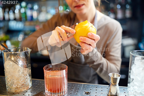 Image of bartender peels orange peel for cocktail at bar