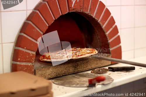 Image of peel taking baked pizza out of oven at pizzeria