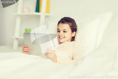 Image of happy girl lying in bed with tablet pc at home