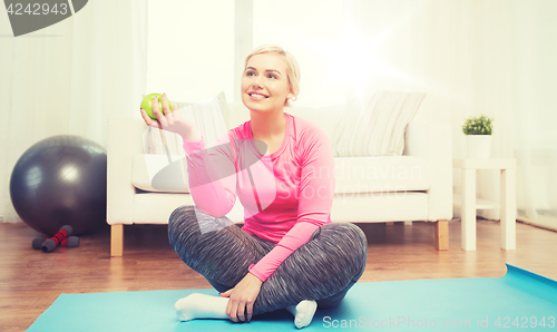 Image of happy woman eating green apple at home