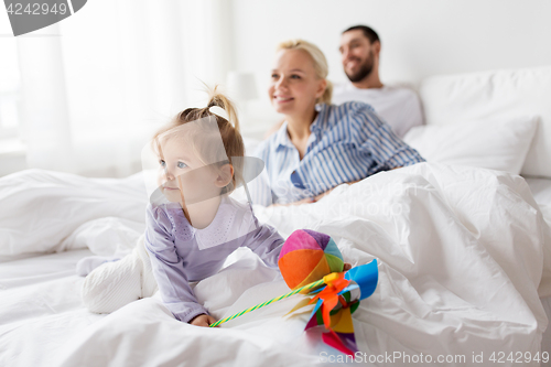 Image of happy child with toys and parents in bed at home