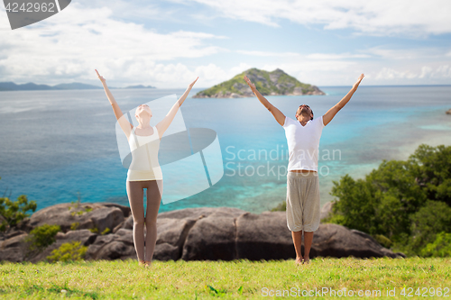 Image of happy couple making yoga exercises on beach