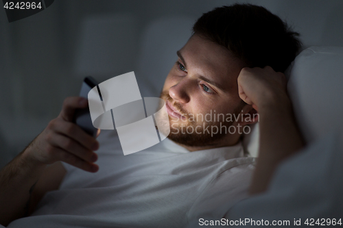 Image of young man with smartphone in bed at night
