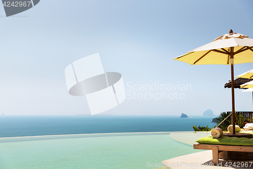 Image of infinity pool with parasol and sun beds at ocean