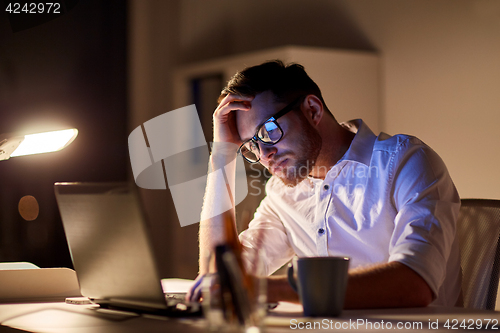 Image of businessman with laptop thinking at night office