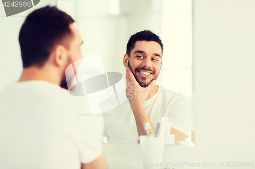 Image of happy young man looking to mirror at home bathroom