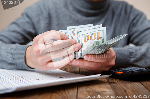 Image of Caucasian hands counting dollar banknotes on dark wooden table