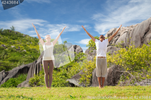 Image of happy couple making yoga exercises on beach