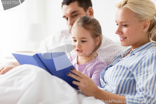 Image of happy family reading book in bed at home