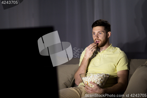 Image of man watching tv and eating popcorn at night