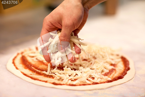 Image of cook hand pouring cheese to pizza at pizzeria