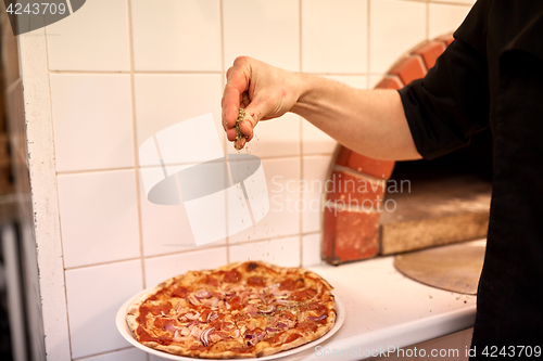 Image of cook adding pepper to salami pizza at pizzeria