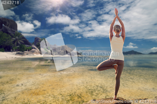 Image of young woman making yoga tree pose over beach