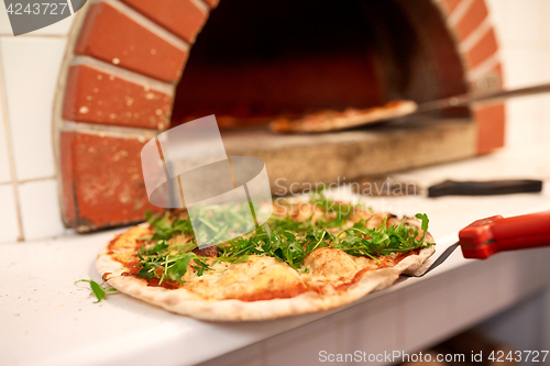 Image of baked pizza on peel at pizzeria oven 