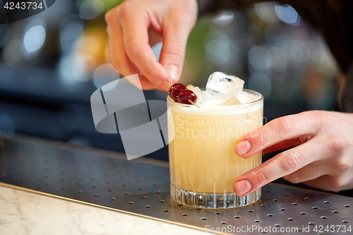 Image of bartender with glass of cocktail and cherry at bar