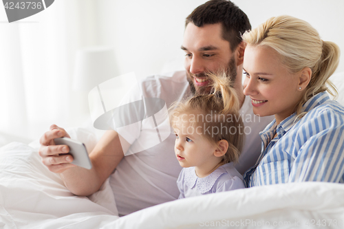 Image of happy family with smartphone in bed at home