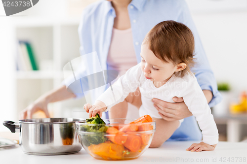 Image of happy mother and baby cooking vegetables at home