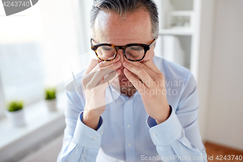 Image of businessman in glasses rubbing eyes at office