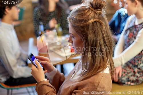 Image of woman with smartphone and friends at restaurant