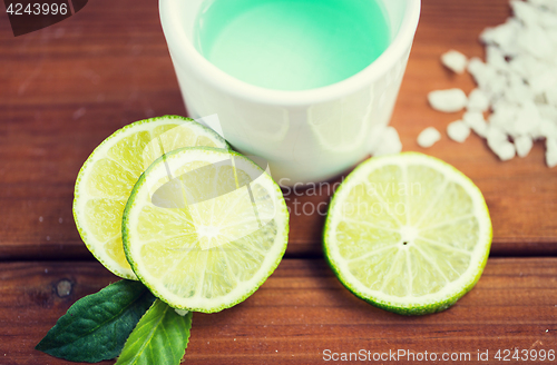 Image of close up of body lotion in cup and limes on wood