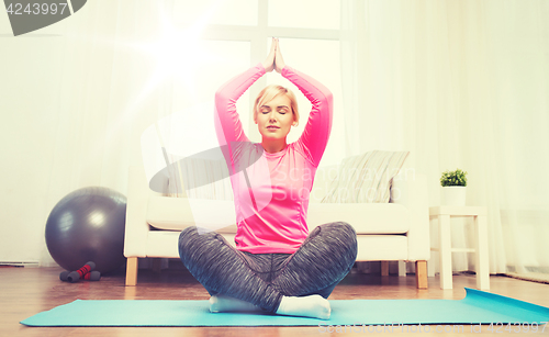 Image of happy woman stretching leg on mat at home