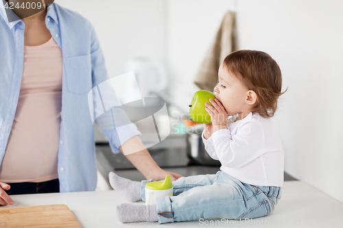 Image of mother and baby eating green apple at home kitchen