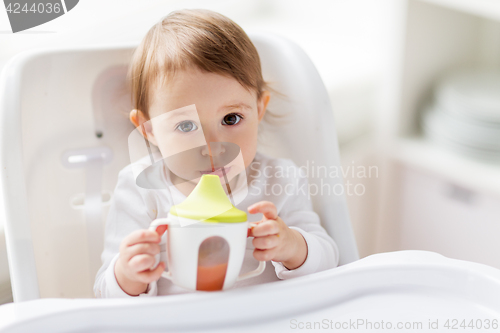 Image of baby drinking from spout cup in highchair at home