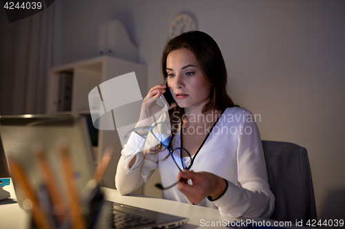 Image of woman with laptop calling on smartphone at office