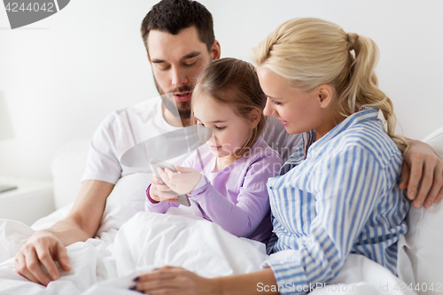 Image of happy family with smartphone in bed at home
