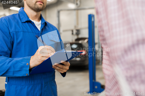 Image of auto mechanic with clipboard and man at car shop