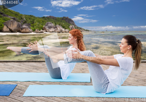 Image of women making yoga in half-boat pose outdoors