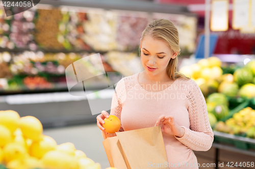 Image of pregnant woman with bag buying oranges at grocery