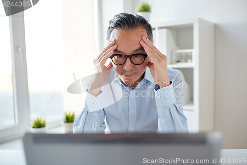 Image of businessman in eyeglasses with laptop at office