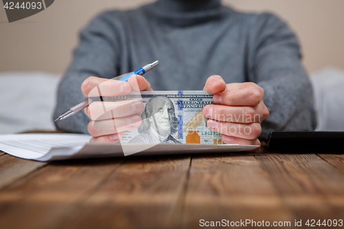 Image of Caucasian hands counting dollar banknotes on dark wooden table