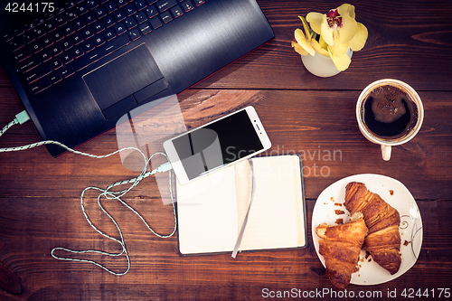 Image of Workspace with laptop, smartphone, croissant, cofee on a wooden 
