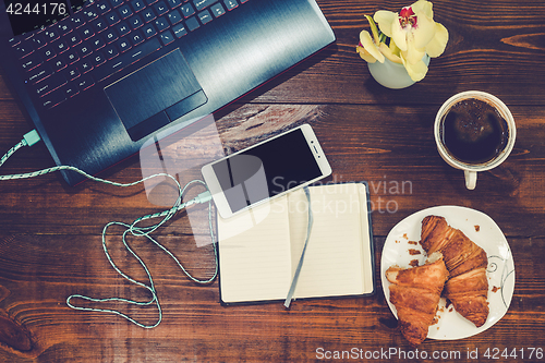 Image of Workspace with laptop, smartphone, croissant, cofee on a wooden 