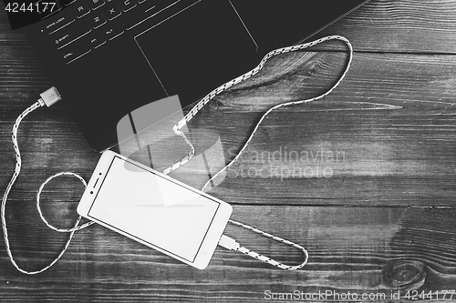 Image of Workspace with laptop and charging blank smartphone on wooden de