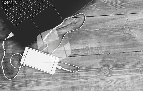 Image of Workspace with laptop and charging blank smartphone on wooden de