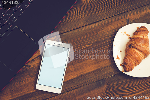 Image of Workspace with laptop, smartphone and croissant on wooden desk