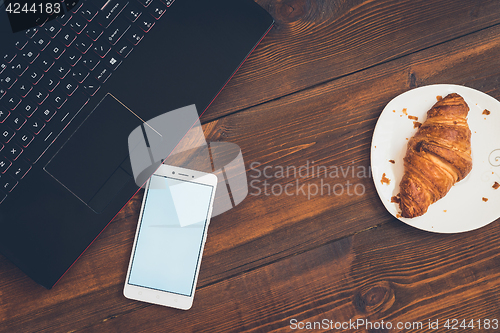 Image of Workspace with laptop, smartphone and croissant on wooden desk