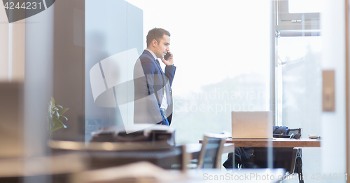 Image of Businessman talking on a mobile phone while looking through window.