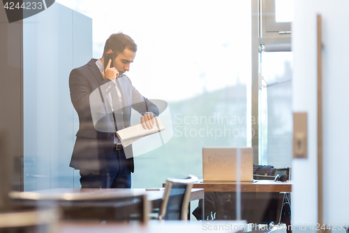 Image of Businessman talking on a mobile phone while looking at wristwatch.