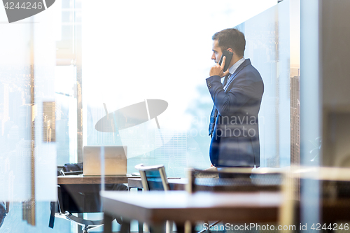 Image of Businessman talking on a mobile phone while looking through window in NY