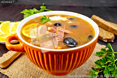 Image of Solyanka with lemon and black olives in bowl on dark board