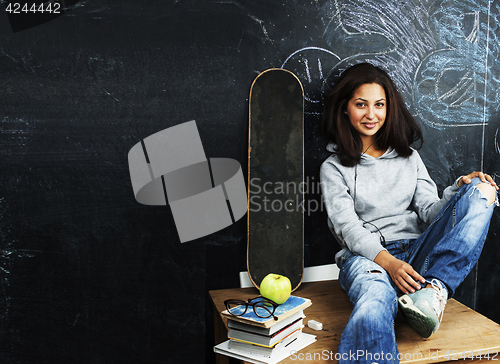 Image of young cute teenage girl in classroom at blackboard seating on ta