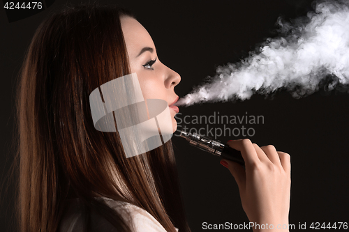 Image of The face of vaping young woman at black studio