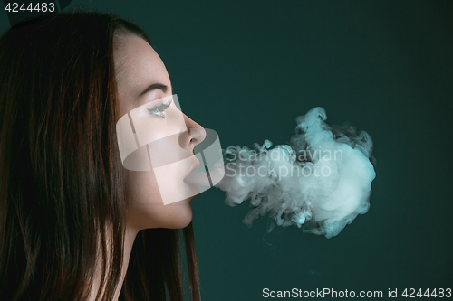 Image of The face of vaping young woman at black studio