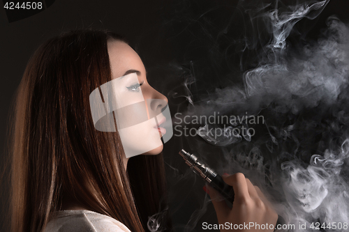 Image of The face of vaping young woman at black studio