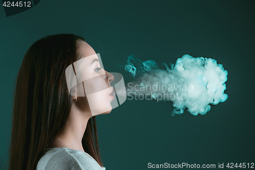 Image of The face of vaping young woman at black studio