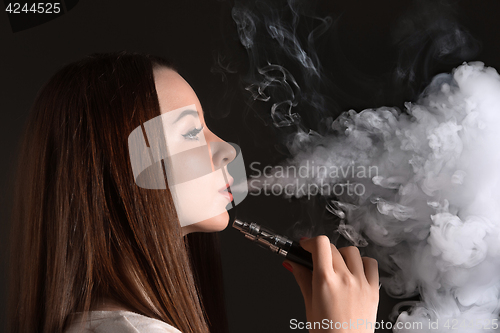 Image of The face of vaping young woman at black studio